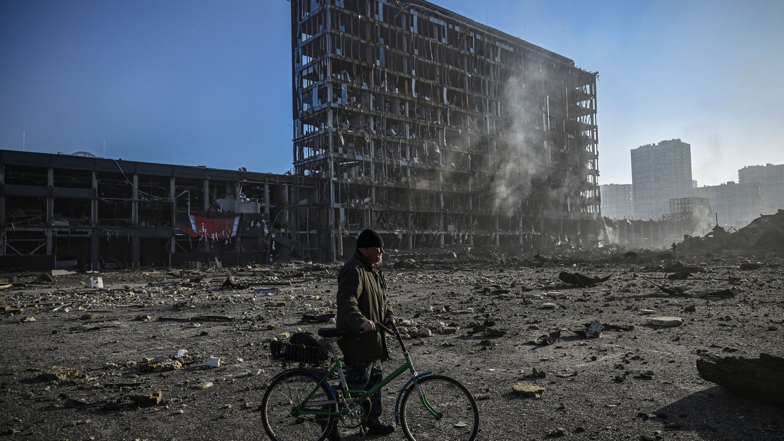 Image - A man with his bicycle walks through debris outside a destroyed shopping centre in Kyiv