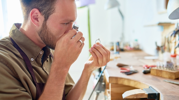 f jeweler inspecting ring through magnifying glass in workshop