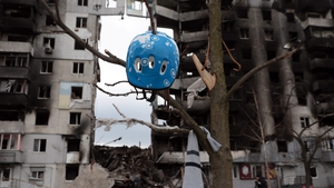 A bicycle helmet hangs on a tree against the background of a residential building damaged by Russian shelling in Borodyanka