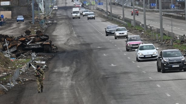 A convoy of cars evacuating civilians passes a destroyed Russian tank on the outskirts of Buzova village, Kyiv region