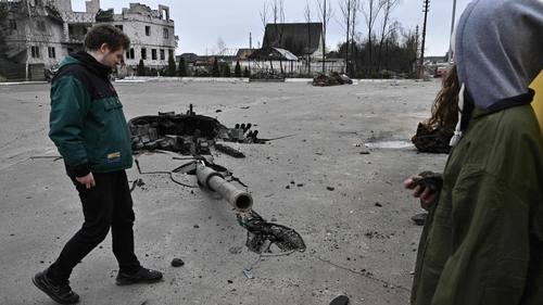 People walk next to the debris of a destroyed Russian tank near the village of Zalissya, northeast of Kyiv