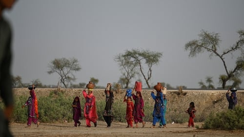 Women walk towards their homes carrying drinking water in containers during a heatwave in Pakistan