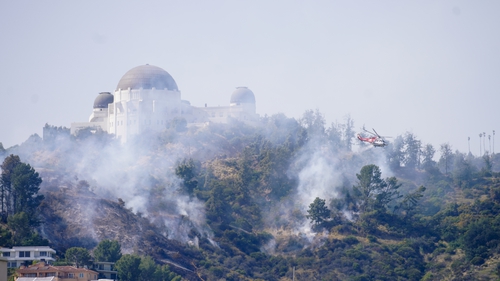 A firefighting helicopter performs a water drop over a brush fire near Griffith Observatory