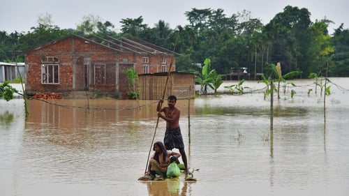 Villagers make their way on a raft past homes in a flooded area after heavy rains in Nagaon district, Assam state