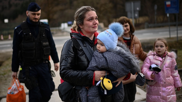 A Polish border guard carries the luggage of a Ukrainian refugee as she holds her baby after crossing the border into Poland