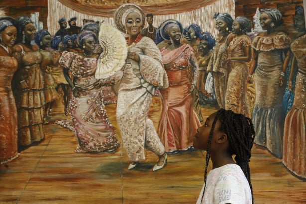 A girl looks up at a painting of women dancing