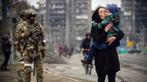 A woman holds a child next to Russian soldiers in Mariupol on 12 April