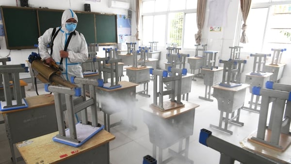 A volunteer wearing sprays disinfectant at an exam site ahead of China's national college entrance exam