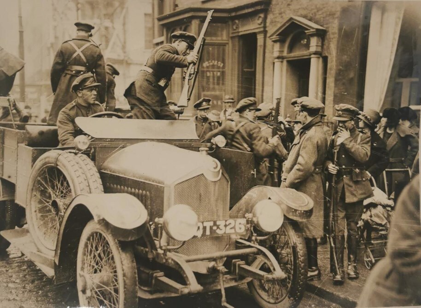 Image - ARREST: Dumbfounded civilians look on as Free State troops swarm Harry Ferguson's Garage to arrest Leo Henderson. (Credit: By permission of Conway's Yard, Oliver Plunkett Street, Cork.)