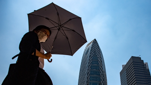 A pedestrian walks with an umbrella to shield from the sun amid a heatwave in Tokyo's Shinjuku district