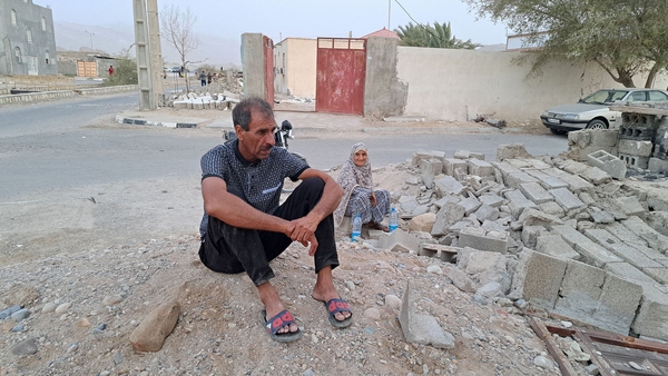 People sit among the rubble in the village of Sayeh Khosh following an earthquake