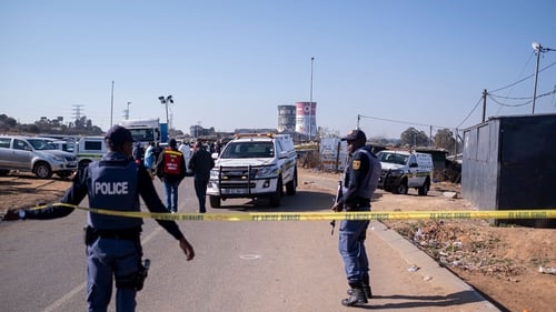 Police officers enforce a perimeter around the crime scene where 14 people where shot dead in Soweto