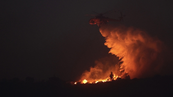 A helicopter drops water over a wildfire north of Athens