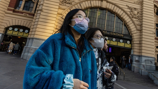 People wearing masks walk in front of Flinders Street Station in Melbourne