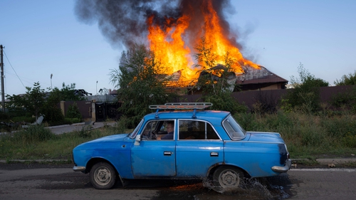 A Ukrainian man drives past a burning house hit by a shell in the outskirts of Bakhmut, eastern Ukraine