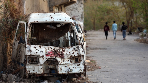 Children walk past a shrapnel-ridden vehicle, in Yemen's third city of Taez