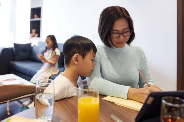 East Asian mother and young son writing a list together at a dining table