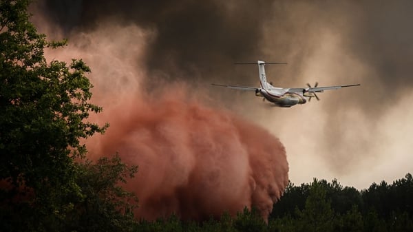 A firefighting aircraft sprays fire retardant over trees during a wildfire near Saint-Magne, southwestern France