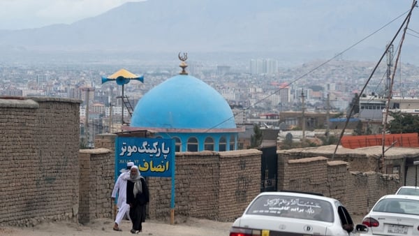 Afghan men walk past the blue dome of a mosque a day after the blast on the outskirts of Kabul
