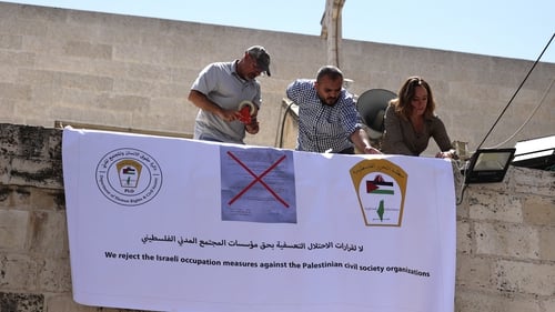 Activists hang a banner outside the Palestinian Al-Haq Foundation in the West Bank city of Ramallah after Israel raided and closed an entrance to their offices on 18 August