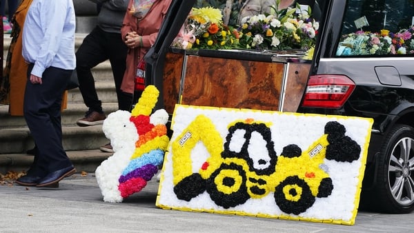 Flowers in the shape of unicorn and a tractor lay on the hearse
