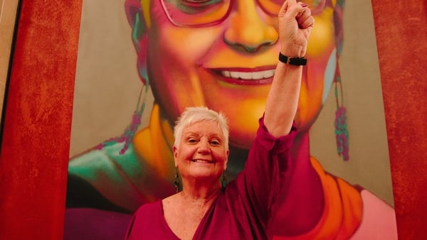 Anne Carr poses in front of her portrait