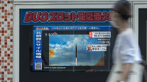 A woman walks past a public television screen in Tokyo, displaying file footage of North Korean missile launches