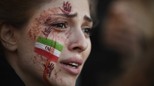 A demonstrator with an Iranian flag and red hands painted on her face attends a rally in support of Iranian protests