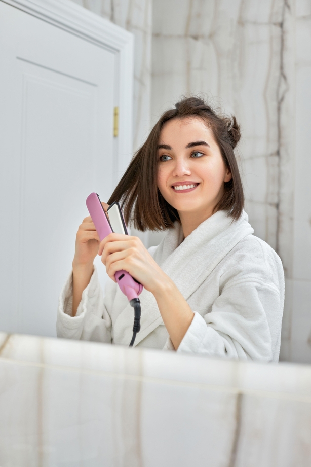 woman using a hair straightener in bathroom.