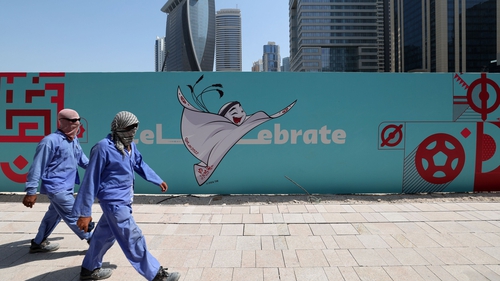 Workers walk past a billboard showing an illustration of the Qatar 2022 FIFA World Cup mascot 'La'eeb' in the Qatari capital Doha