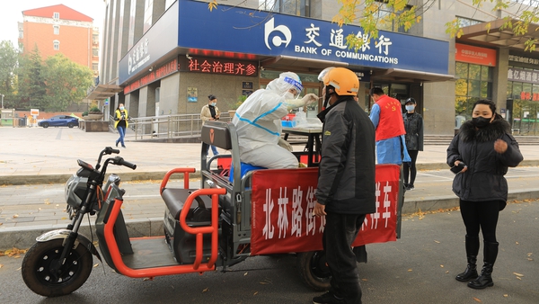 A medical worker sitting on a mobile nucleic acid sampling tricycle takes a swab sample from a resident in Zhengzhou