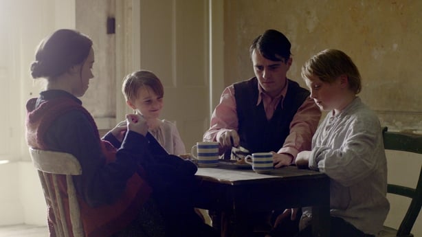 A colour photo of a family sitting around a table in 1920s clothes