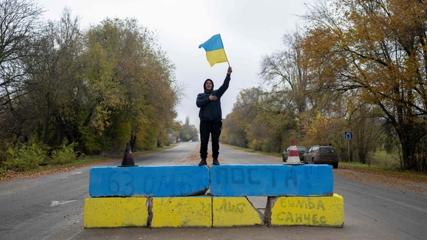 A resident waves a Ukrainian flag at a former Russian checkpoint at the entrance of Kherson as local residents celebrate the liberation of the city, on November 13, 2022
