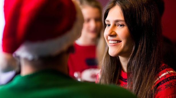 A smiling woman chatting to a male friend in a Santa hat