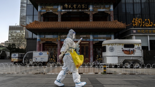 An epidemic control worker walks by a closed business in Beijing, China, today