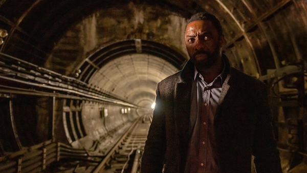 Idris Elba can be seen in an underground tunnel, sporting an inquisitive expression