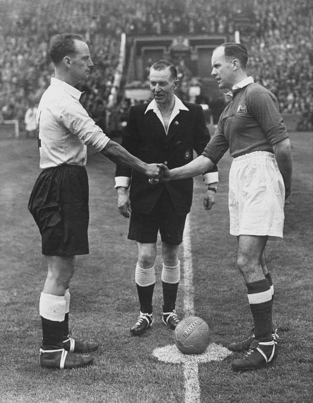Referee Jack Barrick (1900 - 1976) looks on as Manchester United Football Club team captain Johnny Carey (1919 - 1995) and Harry Johnston (1919 - 1973), team captain for Blackpool Football Club (left) shake hands before the kick off of their FA Cup Final match on on 24th April 1948 at Wembley Stadium in London, United Kingdom. Manchester United won the game 4-1 . (Photo by Fox Photos/Hulton Archive/Getty Images).