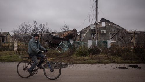 A man rides a bike past a destroyed house on the outskirts of Kherson
