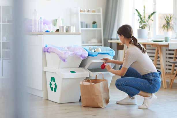 Woman sorting plastic & paper into different bins in kitchen