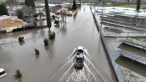A vehicle drives on a flooded roadway in Planada, California