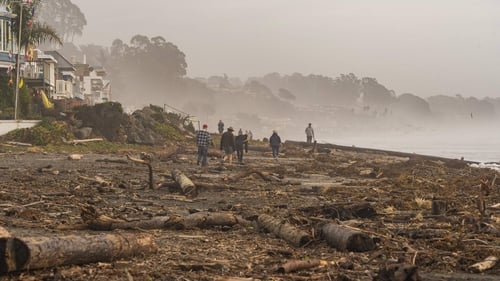 People walk among storm debris on Rio Del Mar beach in Aptos, California