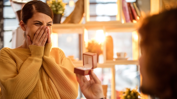 Young surprised woman being proposed by her boyfriend.