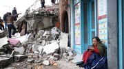 A woman sits on the ground beside demolished buildings in the Iskenderun district of Hatay