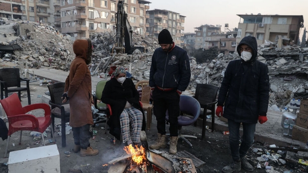 People gather around a fire beside collapsed buildings in Hatay, Turkey