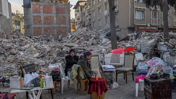 Displaced quake-hit residents sit with their belongings near the collapsed buildings in Hatay