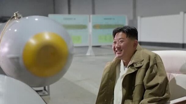Kim Jong-un sitting and smiling in front of a weapon, claimed to be the unmanned underwater nuclear attack craft called 'Haeil'