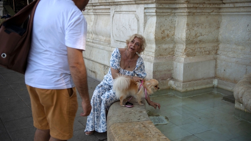 A woman gives water from a fountain to her dog in Seville