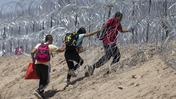 People walk through razor wire surrounding a makeshift migrant camp after crossing the border from Mexico on 11 May