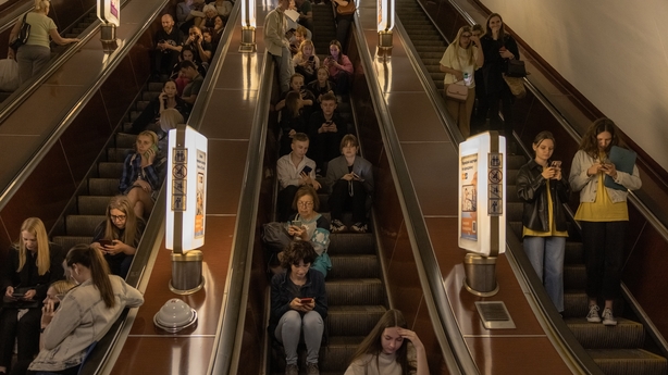 People sit on an escalator as they shelter in a metro station in Kyiv