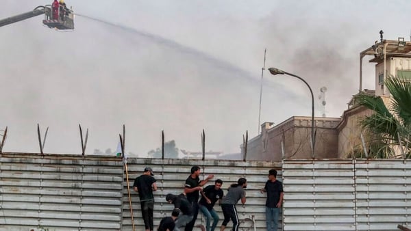 Protesters climb the fence of the Swedish embassy in Baghdad as firefighters try to put out a fire